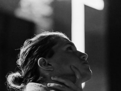 grayscale photography of woman standing near white cross signage