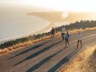 four men and women walking on roadway near body of water